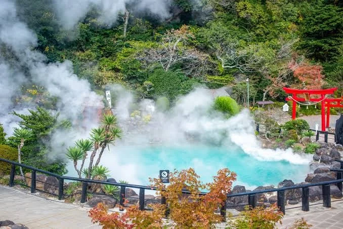 Turquoise geothermal pond with rising steam and a red torii